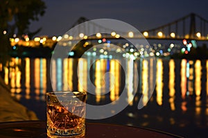 whisky on table, city waterfront with litup bridges beyond