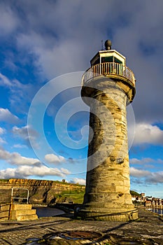 Whitby harbour lighthouse in sumer with blue sky and golden sun