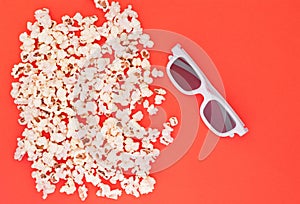 White 3d glasses and fresh cheesy popcorn on a red background, top view, copyspace