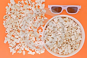 White 3d glasses paper cup and fresh cheesy popcorn on a orange background, top view, copyspace