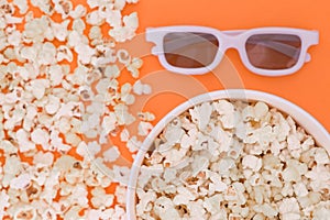 White 3d glasses, paper cup and fresh cheesy popcorn on a orange background, top view, copyspace