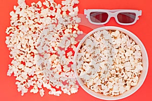 White 3d glasses paper cup and fresh cheesy popcorn on a red background, top view, copyspace