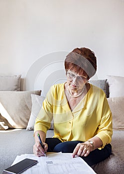 White adult woman in a yellow blouse assorts bills, paper, woman