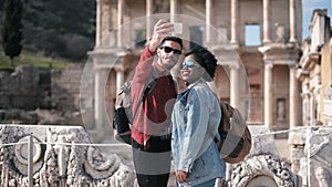 White and African couple taking a selfie in front of the Celcus library.