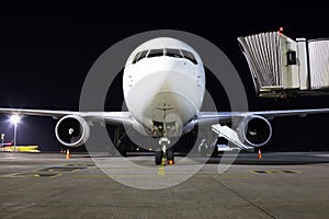 White aircraft on the parking area in the airport at night, front view