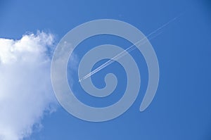 White airplane and its vapour trails on the background of a bright blue sky. Looking up at the sky. Plane flying high in the sky t