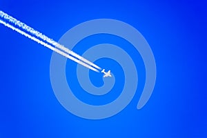 White airplane silhouette with white trail on blue sky