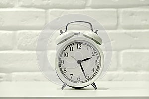 White alarm clock with black dial on brick wall background