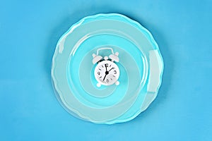 White alarm clock in blue empty plate. Time to lose weight , eating control or time to diet concept