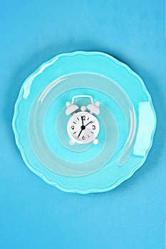 White alarm clock in blue empty plate. Time to lose weight , eating control or time to diet concept