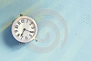 White alarm clock on the blue textured table and sunryses