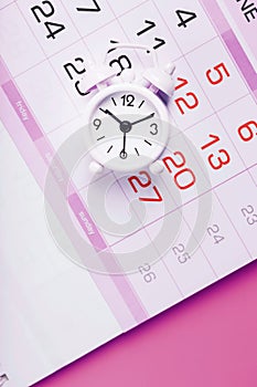 White alarm clock and calendar on a pink desktop background.