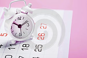 White alarm clock and calendar on a pink desktop background.