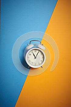 White alarm clock with on divided diagonally blue-yellow background with copy space for your text. Close up