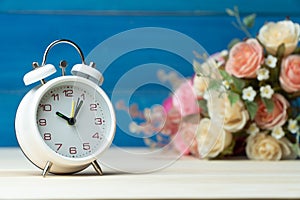 White alarm clock and flowers pink and red rose on wooden table and blue background with copy space for add text and content