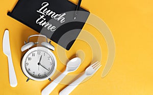 White Alarm clock with knife fork and spoon for mealtime or diet concept on yellow background, free space for text.