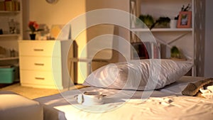 White alarm clock lying on messy bed, crumpled bed sheets, oversleeping concept