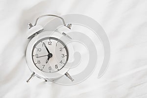 White alarm clock on messy  bed sheet , early wake up , awaken  or reminder concept with copy space