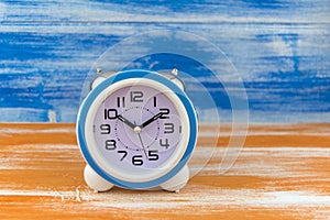 White alarm clock on a orange wooden table on blue wall background