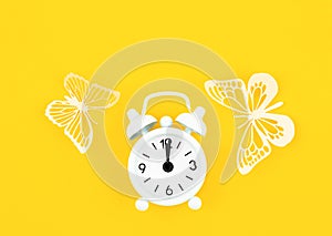 The White alarm clock and paper butterflies on a yellow background