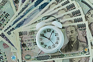 white alarm clock on pile of japanese yen banknotes as time count down or deadline concept