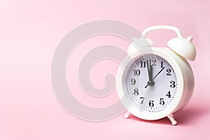 White alarm clock on pink background, copy space. Minimalistic background, concept of time, deadline, time to work, morning