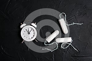 White alarm clock with sanitary female tampons on black background