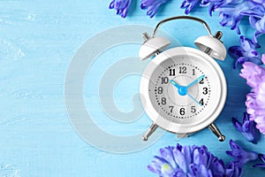 White alarm clock, spring flowers and space for text on blue wooden table, flat lay. Time change