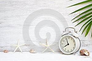 White alarm clock with starfish, sea shells and green palm leaf background. Background concept for Summer time holiday vacation.