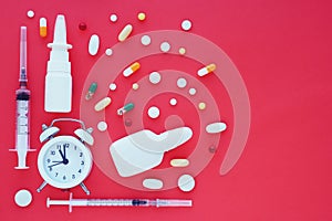 White alarm clock, syringes, pills and nasal sprays on a bright red background.