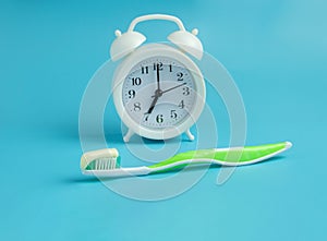 White alarm clock, toothbrush and toothpaste on light blue table background. Dental and healthcare concept