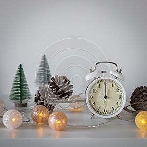 white alarm clock, a twelve pointer, a small artificial green Christmas tree and garland on a white chest of drawers. Copy space