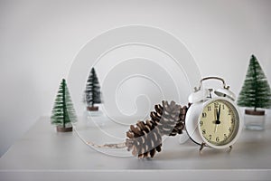 White alarm clock,  twelve pointer, a small artificial green Christmas tree on a white chest of drawers. Copy space. Christmas