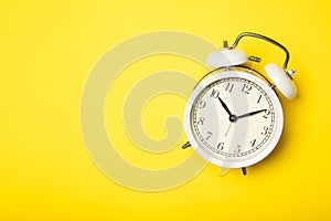 White alarm clock on a yellow background. Top view, place for text
