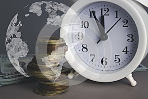 White alarmclock with Coins stack and stack of one hundred dollar bills with Digital Earth planet Global world map symbol on grey