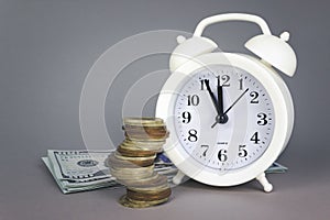 White alarmclock with Coins stack and stack of one hundred dollar bills on grey background. Interest rate, dividend concept,