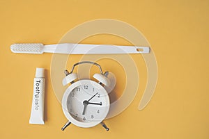 White analog alarm clock , tube of toothpaste and toothbrush on grunge yellow background