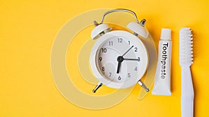 White analog alarm clock , tube of toothpaste and toothbrush on grunge yellow background , cleaning teeth and mouth