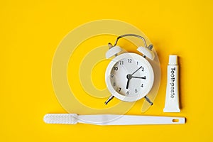 white analog alarm clock , tube of toothpaste and toothbrush on grunge yellow background , cleaning teeth and mouth concept