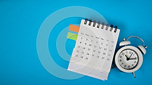 White analog alarm clock on white calendar with grunge blue background with copy space, business meeting schedule