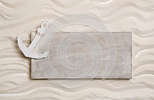 White anchor with a wooden sign in the sand. Background for crui
