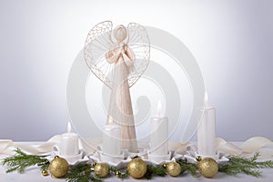 A white angel and four white Advent candles, Christmas tree branches are decorated with golden balls. The imminent