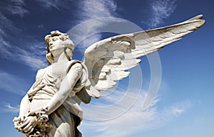 Angel. White guardian angel marble sculpture with open long wings on a bright sunny blue sky