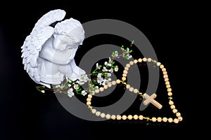 White angels statue with white flowers on black background and wooden rosary