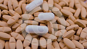 White antipyretic capsules fall on bright orange antibiotics slow motion rotate