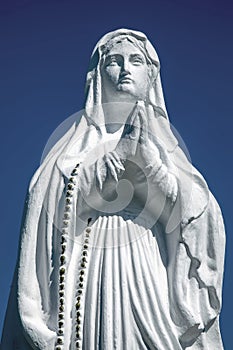 White antique statue of Virgin Mary praying against blue sky. Copy space. Vertival image