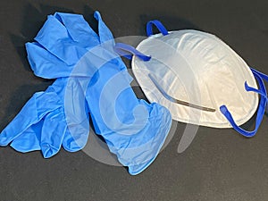 White antivirus mask and blue latex gloves on dark background.