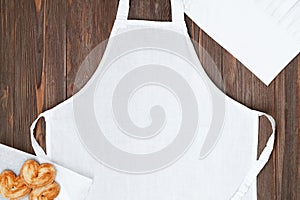 White apron template on brown wooden table with cookies, copy space. Kitchen, cooking clothing mockup photo