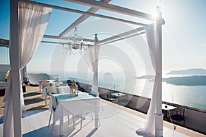 White arch for a wedding ceremony in the open air with lanterns and a platform with white furniture on the background of the sea,