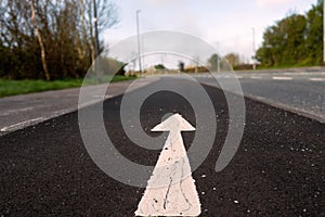 White arrow on a black asphalt surface in focus. Direction sign on a road